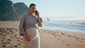 Expectant mother talking cellphone walking evening beach looking ocean waves. Royalty Free Stock Photo