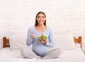 Expectant Woman Eating Salad Smiling At Camera Sitting On Bed