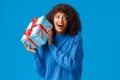Expectations, holidays and winter concept. Excited cheerful african-american woman shaking box with gift, want unwrap