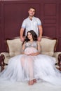 In expecting. Happy pregnant pair in fashion clothes posing in studio