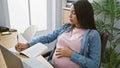 Expecting young hispanic businesswoman, task-juggling in her profession, sensitively balancing pregnancy and work - note-taking on Royalty Free Stock Photo