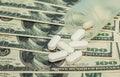 Expensive medicine. Covid-19 coronavirus pills are scattered across the hundred dollar bills. A handful of pills on Royalty Free Stock Photo