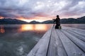 Experience nature with the hobby of outdoor photography - A man kneeling on a wooden pier of a lake adjusts his camera aiming at a Royalty Free Stock Photo