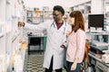 Experienced African American man pharmacist consulting female customer in modern pharmacy