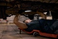 experienced auto mechanic male working alone on floor repairing bottom of car