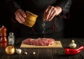 Experienced chef sprinkles raw meat with salt. Preparing beef meat before baking. Working environment in the kitchen Royalty Free Stock Photo