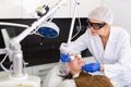 Female cosmetologist performing laser facial treatment to elderly woman