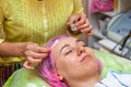 An experienced cosmetologist applies a mask of emulsion on the face of a young girl who lies on the couch during facial cleansing