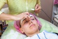 An experienced cosmetologist applies a mask of white cream on the face of a young girl who lies on the couch during facial