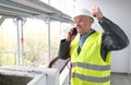 Experienced elderly builder, construction team chief, construction engineer in helmet protection talking on phone at construction