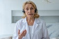 An experienced elderly female doctor who talks into the camera and gives online medical advice in a private clinic.