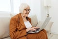 an experienced, elderly woman is sitting on a sofa in a brown suit, holding a video conference on a laptop, passing on