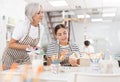 Experienced female ceramicist teaching young girl to paint ceramics in pottery studio Royalty Free Stock Photo