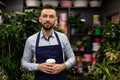 an experienced florist in a blue apron surrounded by flowers and bouquets stands smiling and looks at the camera