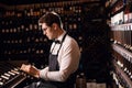 Male wine steward looks at bottles of wine and writing in notebook at wine store