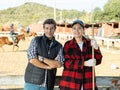 Experienced man and woman in plaid shirts looking at camera while holding working tool on horse ranch in spring Royalty Free Stock Photo