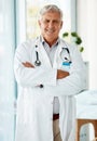 Experienced mature male doctor smiling and standing with his arms crossed in a hospital. One optimistic senior man Royalty Free Stock Photo