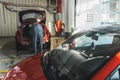 Experienced mechanic diagnoses and repairs a red car in a busy auto repair shop