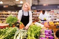 Experienced middle aged saleswoman working in organic food store, arranging fresh vegetables on counter