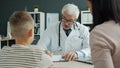 Experienced paediatrist talking to mother and child writing in medical record in clinic