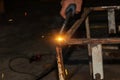 An experienced person performs work with a welding machine, fixing metal parts, removing blue smoke and yellow sparks and