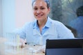 Experienced female pharmacologist smiles at camera while examining a chemical on a Petri dish using a magnifying glass