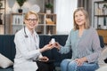 Experienced pleasant smiling woman doctor, giving bottle of pills to her sick female patient, prescribing treatment