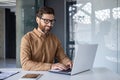 Experienced programmer inside office at workplace, senior man with beard and glasses working on laptop, businessman