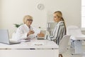Experienced senior doctor giving prescription to young patient sitting at desk in hospital office Royalty Free Stock Photo