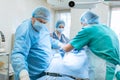 An experienced surgeon in a mask and gown operates in a sterile operating room with an assistant and an anesthesiologist..A group