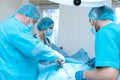 An experienced surgeon in a mask and gown operates in a sterile operating room with an assistant and an anesthesiologist..A group