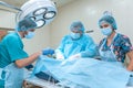 An experienced surgeon in a mask and gown operates in a sterile operating room with an assistant and an anesthesiologist..A group