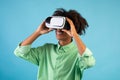 Experiencing futuristic technologies. Black guy wearing and touching VR headset, exploring cyberspace, blue background Royalty Free Stock Photo