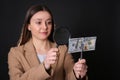 Expert authenticating 100 dollar banknote with magnifying glass against black background, focus on hand. Fake money