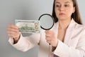 Expert authenticating 100 dollar with magnifying glass against light grey background, focus on hand. Fake money concept