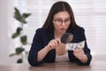 Expert authenticating dollar banknote with magnifying glass at table in office, focus on hand. Fake money concept