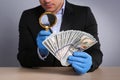 Expert authenticating 100 dollar banknotes with magnifying glass at table on light grey background, closeup. Fake money concept Royalty Free Stock Photo