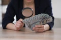 Expert authenticating 100 dollar banknotes with magnifying glass at table in office, closeup. Fake money concept