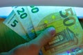 Expert checks paper euro banknotes with infrared or ultraviolet light detector.