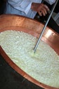 expert cheesemaker stirs the curds into the copper cauldron to m