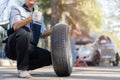 Expertise mechanic man in uniform holding a tire for help a woman for changing car wheel on the highway, car service, repair, Royalty Free Stock Photo