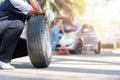 Expertise mechanic man in uniform holding a tire for help a woman for changing car wheel on the highway, car service, repair, Royalty Free Stock Photo