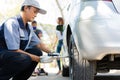 Expertise mechanic man  in uniform using force trying to unscrew the wheel bolts nuts and help a woman for changing car wheel on Royalty Free Stock Photo