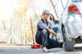 Expertise mechanic man  in uniform using force trying to unscrew the wheel bolts nuts and help a woman for changing car wheel on Royalty Free Stock Photo