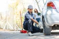 Expertise mechanic man  in uniform using force trying to unscrew the wheel bolts nuts and help a woman for changing car wheel on Royalty Free Stock Photo