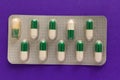 Expired white and green capsules in medicine box. Pills over purple background. Royalty Free Stock Photo