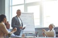 Explaining business strategy. Confident mature businessman standing near flipchart, giving a presentation while having a Royalty Free Stock Photo