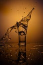 Exploding Glass cup with water shattering over orange background.