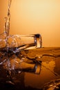 Exploding Glass cup with water shattering over orange background.