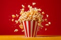 Exploding Popcorn In A Striped Bucket With Dynamic Motion On Red Background. Generative AI